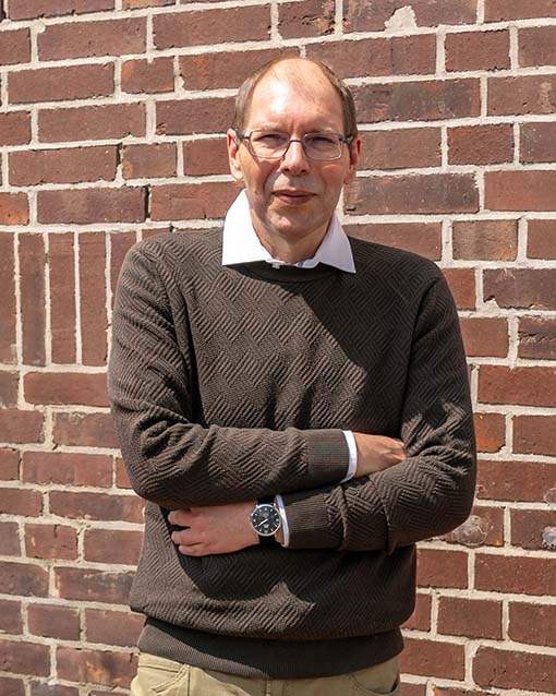 Der erfolgreiche Umschüler André Pardun steht mit verschränkten Armen vor einer geziegelten Hauswand.