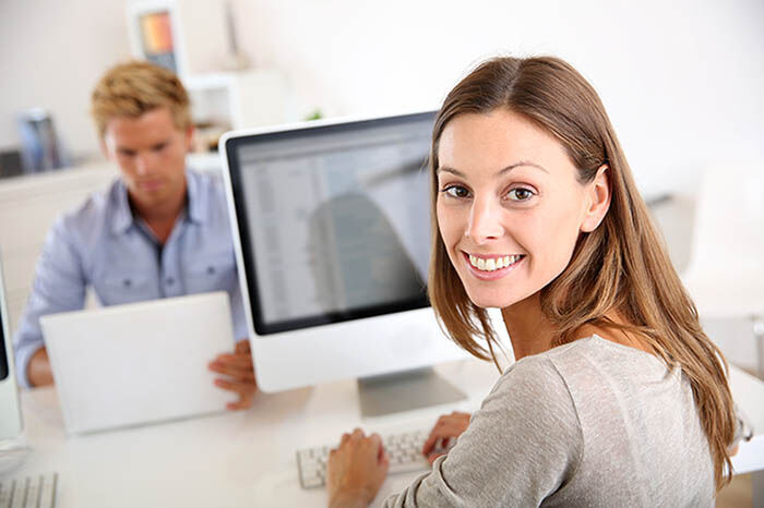 eine Frau, die an einem Schreibtisch mit einem Computer sitzt und mit einer anderen Frau spricht