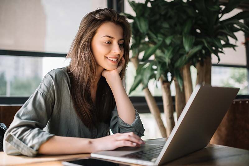 Junge Frau sitzt am Laptop und schaut zufrieden